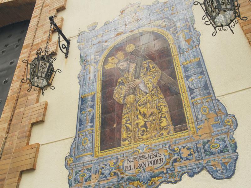 Azulejo multicolor con dos faroles a cada lado de la imagen del Gran Poder en la facha de la iglesia de la Calle Real, como comúnmente de la conoce.