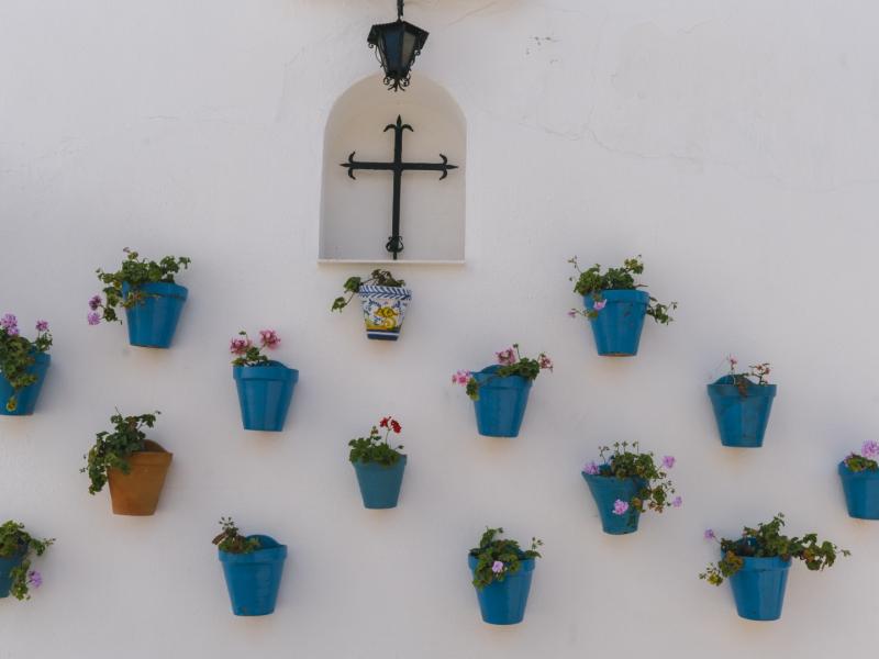 Macetas colgadas en la pared con flores,  una cruz y un farolillo