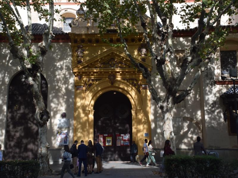Imagen más cerca de la puerta de entrada principal de la real parroquia de santa maría magdalena con personas en la puerta y los árboles dando sombra a la fachada