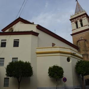 Edificación de la iglesia de san gil abad donde se ve el edificio completo con la torre y el campanario, delante de la entrada hay varios árboles