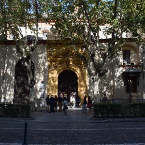Imagen de la fachada de la real parroquia de santa maría magdalena, donde se ve grupos de personas esperando para entrar y árboles tapando parte del edificio