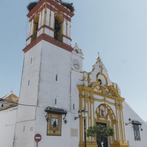Fachada principal de la parroquia, con la torre, nidos de cigüeñas, reloj, azulejos y bancos