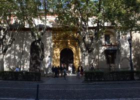 Imagen de la fachada de la real parroquia de santa maría magdalena, donde se ve grupos de personas esperando para entrar y árboles tapando parte del edificio