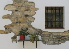 El Ronquillo. Macetas en una fachada de casa blanca con ventana y piedra vista